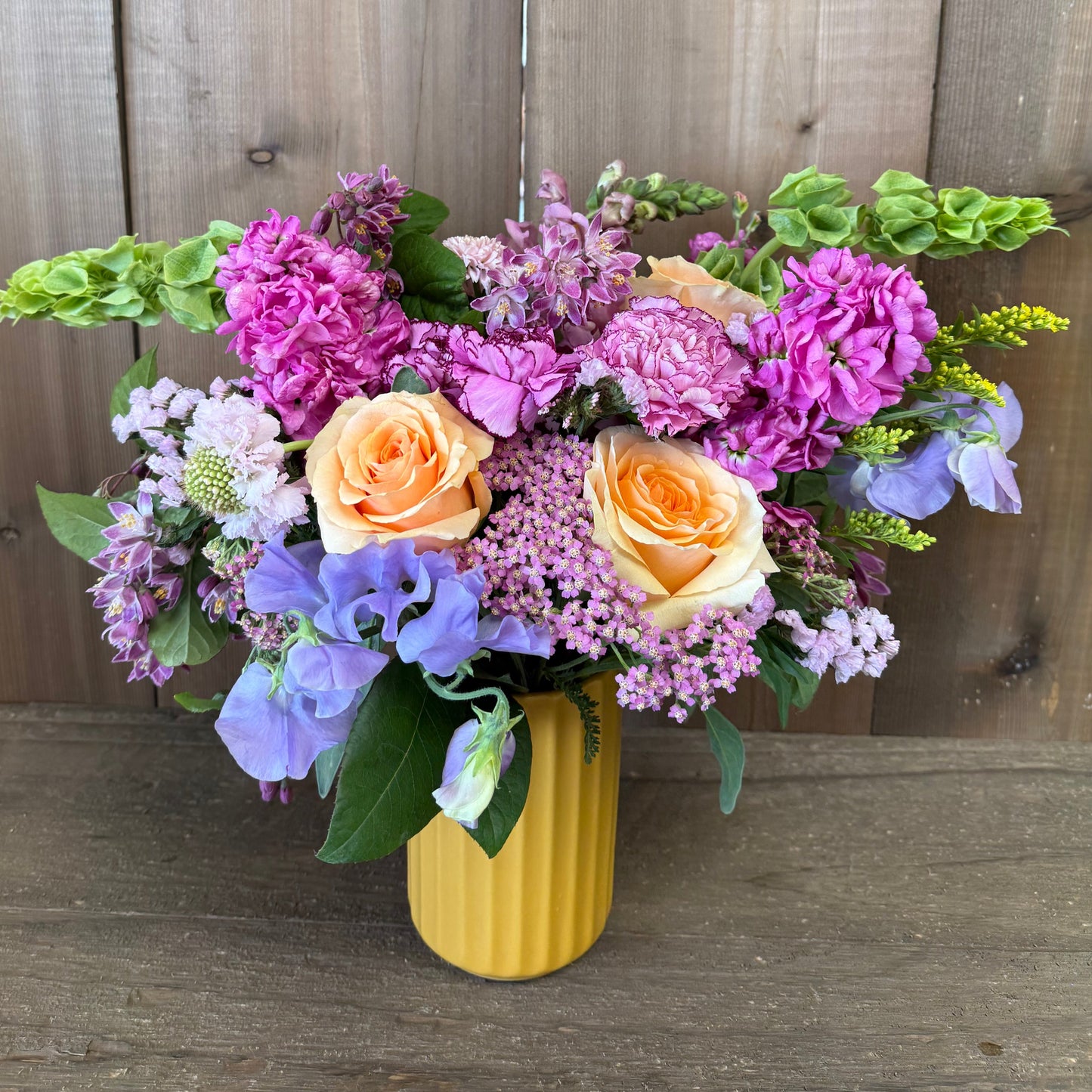 Bouquet of flowers in a yellow vase against a wooden background